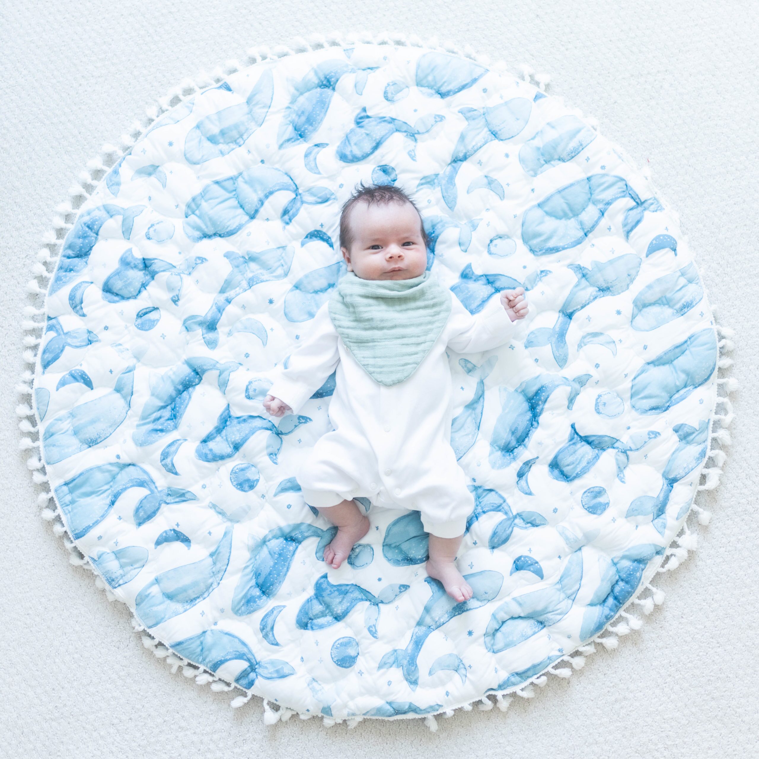 Baby wearing a blue bib while lying on a whale playmat