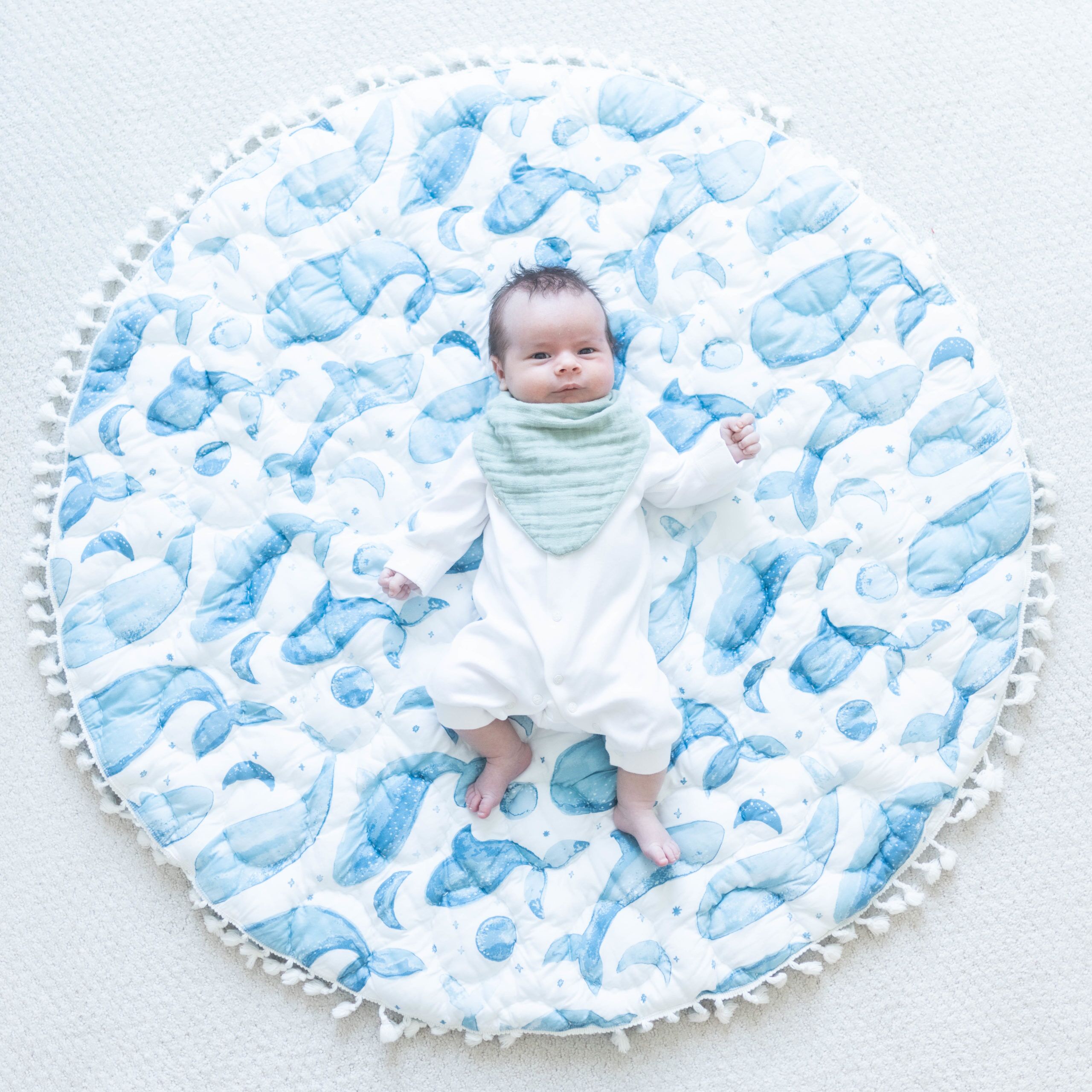 Baby wearing a blue bib while lying on a whale playmat